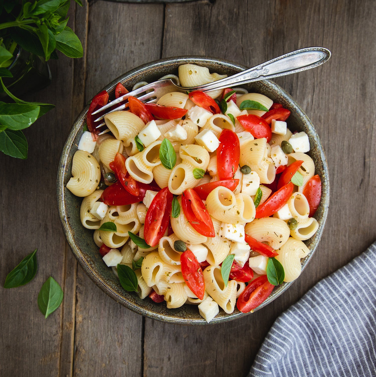 Top-down of Organic Durum Semolina Chiocciole pasta in a bowl with cherry tomatoes, mozzarella, basil on wooden table