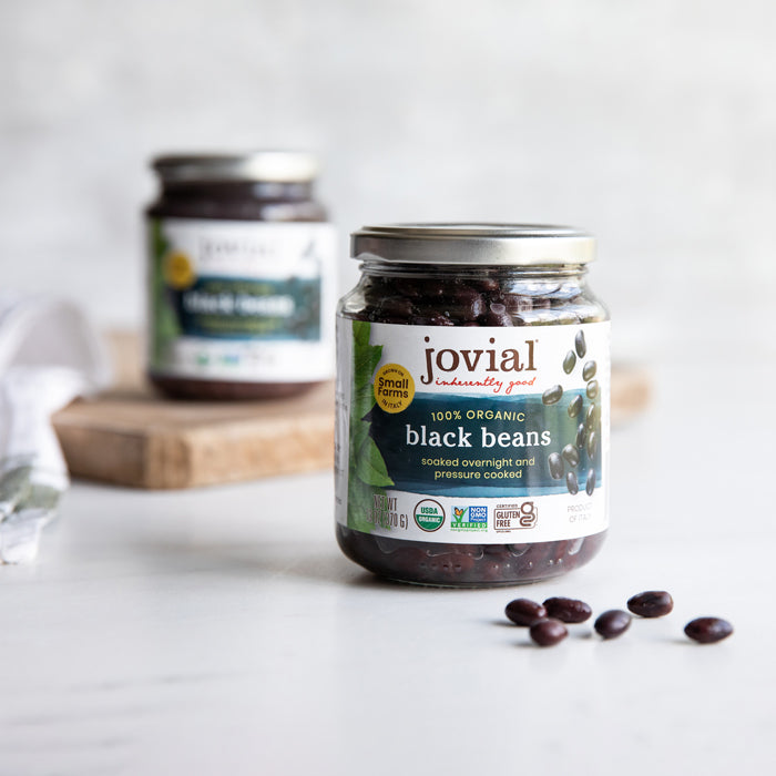 Front view of Jovial organic black beans jar showing the label and a few beans on a white countertop