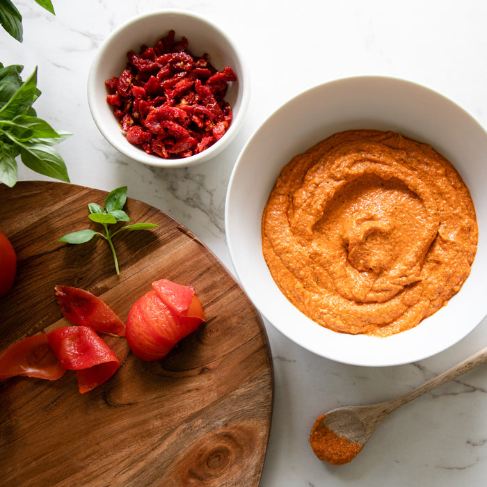Creamy sun-dried tomato dressing in a bowl with chopped sun-dried tomatoes, fresh basil, and a wooden spoon on a marble countertop