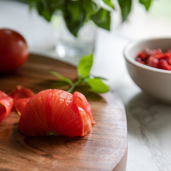 Peeled fresh tomato skin curled on a wooden cutting board with basil and a bowl of chopped tomatoes in natural light
