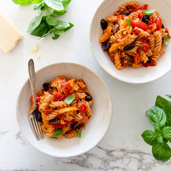 Overhead view of two bowls of Italian sun-dried tomato fusilli pasta salad with olives, cherry tomatoes and basil on marble