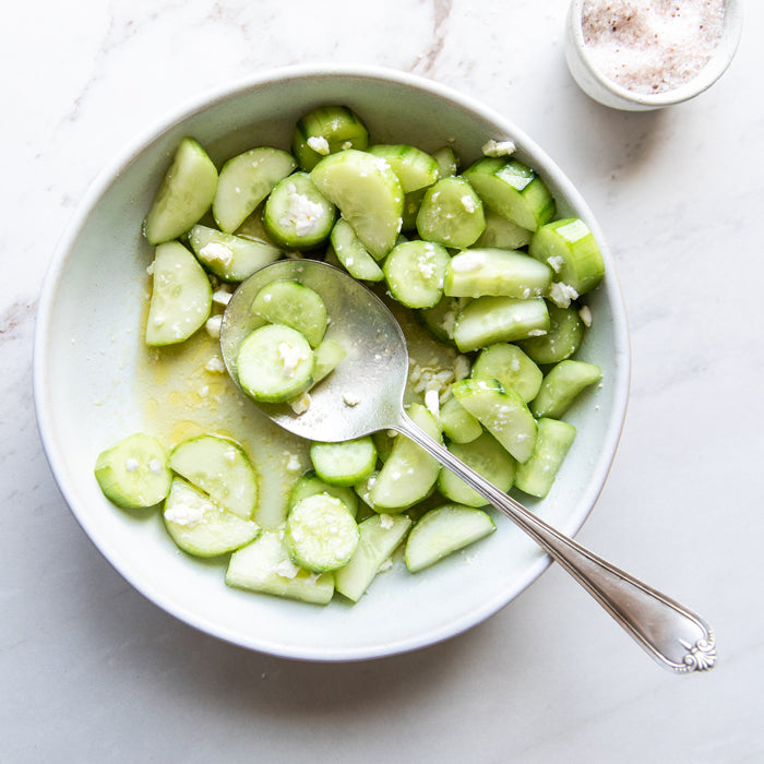 Overhead view of cucumber and goat cheese salad in a white bowl with olive oil on a marble surface