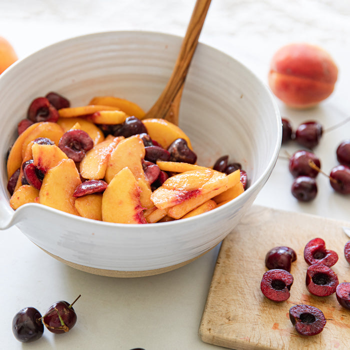 Bowl of sliced peaches and halved cherries tossed for an Einkorn summer fruit crumble on a light countertop