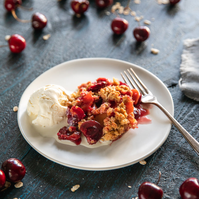 Einkorn summer fruit crumble with cherries and vanilla ice cream on a white plate over a dark wood table