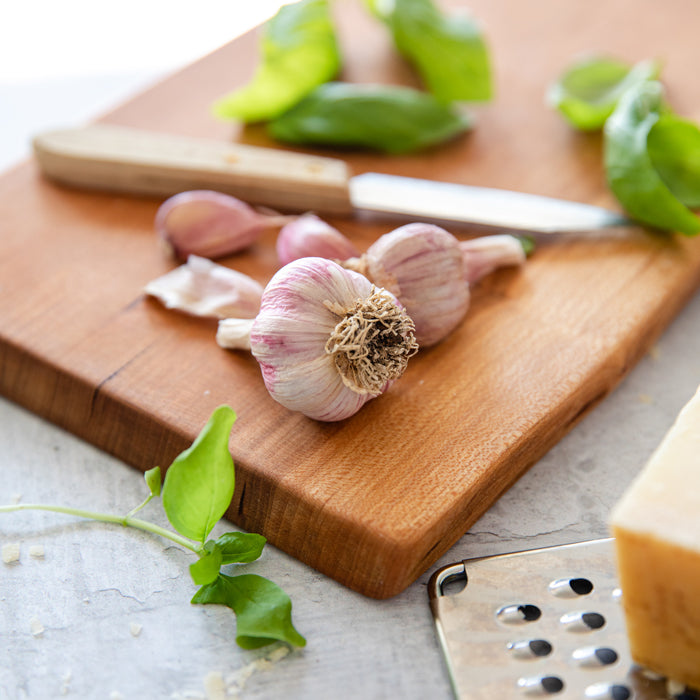 Garlic bulbs on a wooden cutting board with a knife, basil leaves, and Parmesan, ingredients for grain-free orzo risotto
