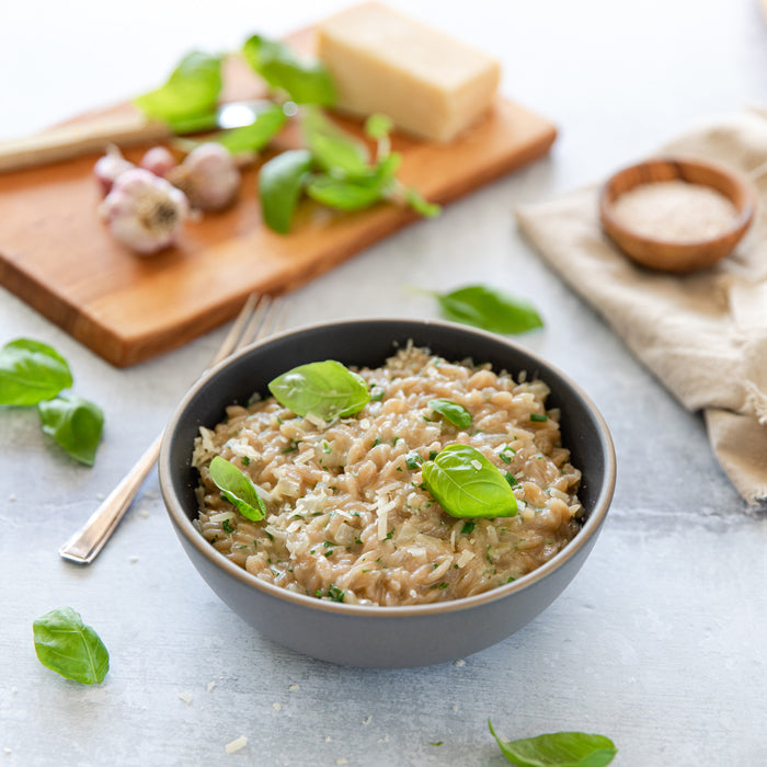 Top-down view of grain-free orzo risotto in a bowl showcasing creamy texture, shaved cheese, and fresh basil garnish on a light tabletop