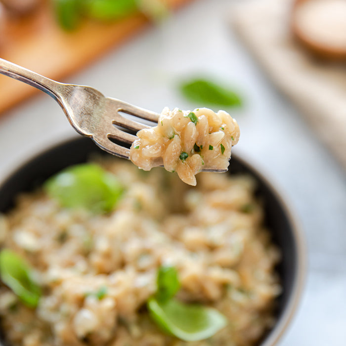 Fork lifting a bite of grain-free orzo risotto with fresh herbs above a bowl