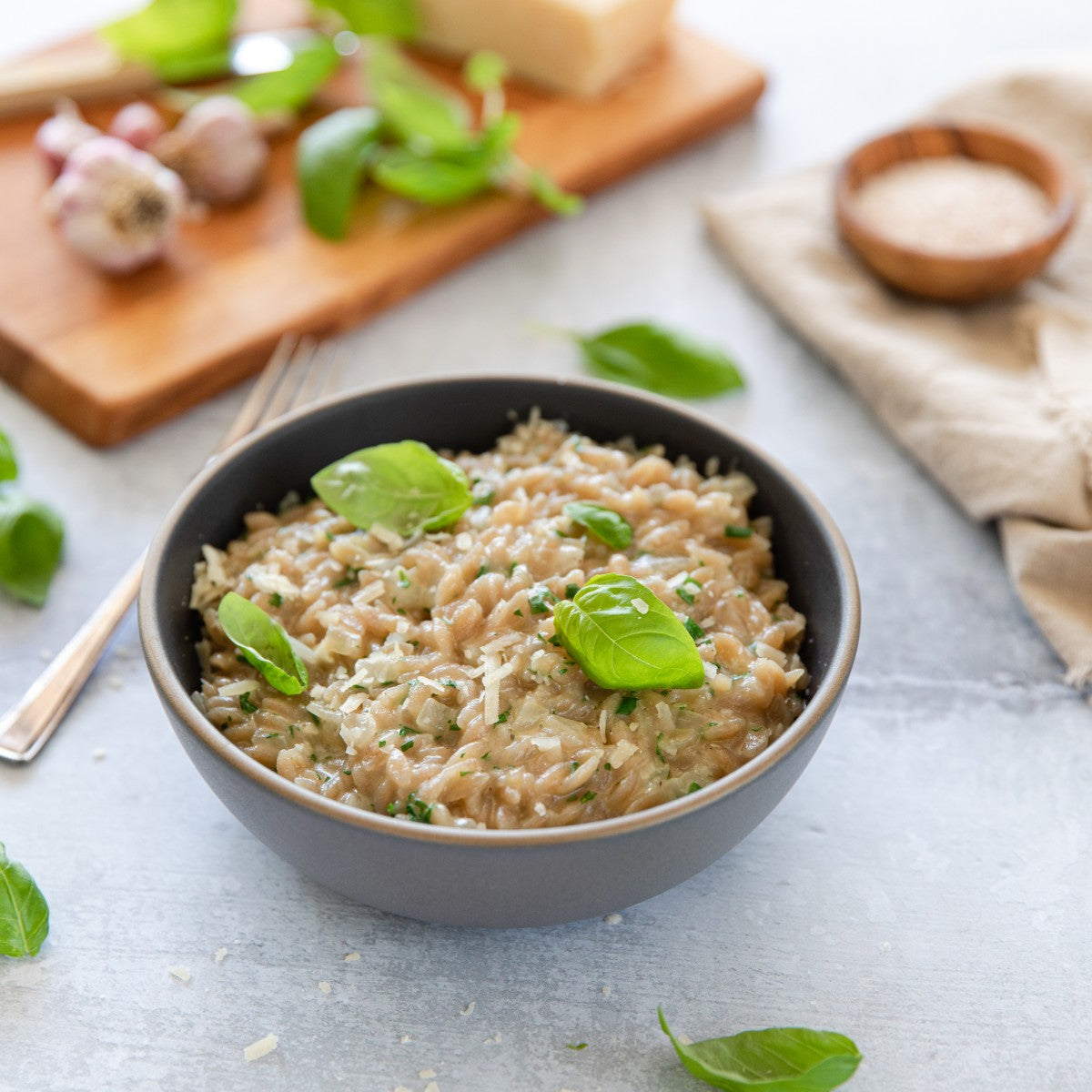 Bowl of herbed risotto made from organic brown rice orzo, garnished with basil and grated cheese on a light tabletop