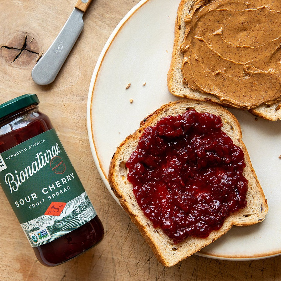 Jar of organic strawberry fruit spread beside a slice of toast topped with jam on a plate on a wooden table