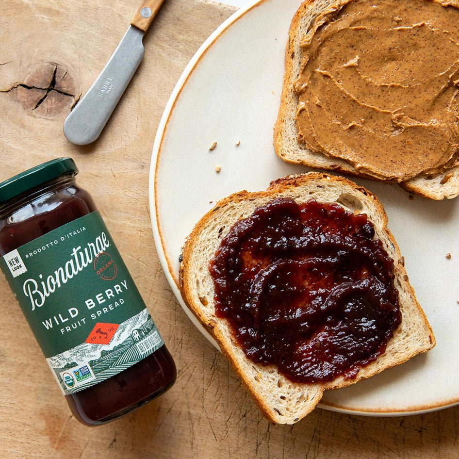 Jar of Bionaturae organic wild berry fruit spread next to toast topped with jam on a wooden board