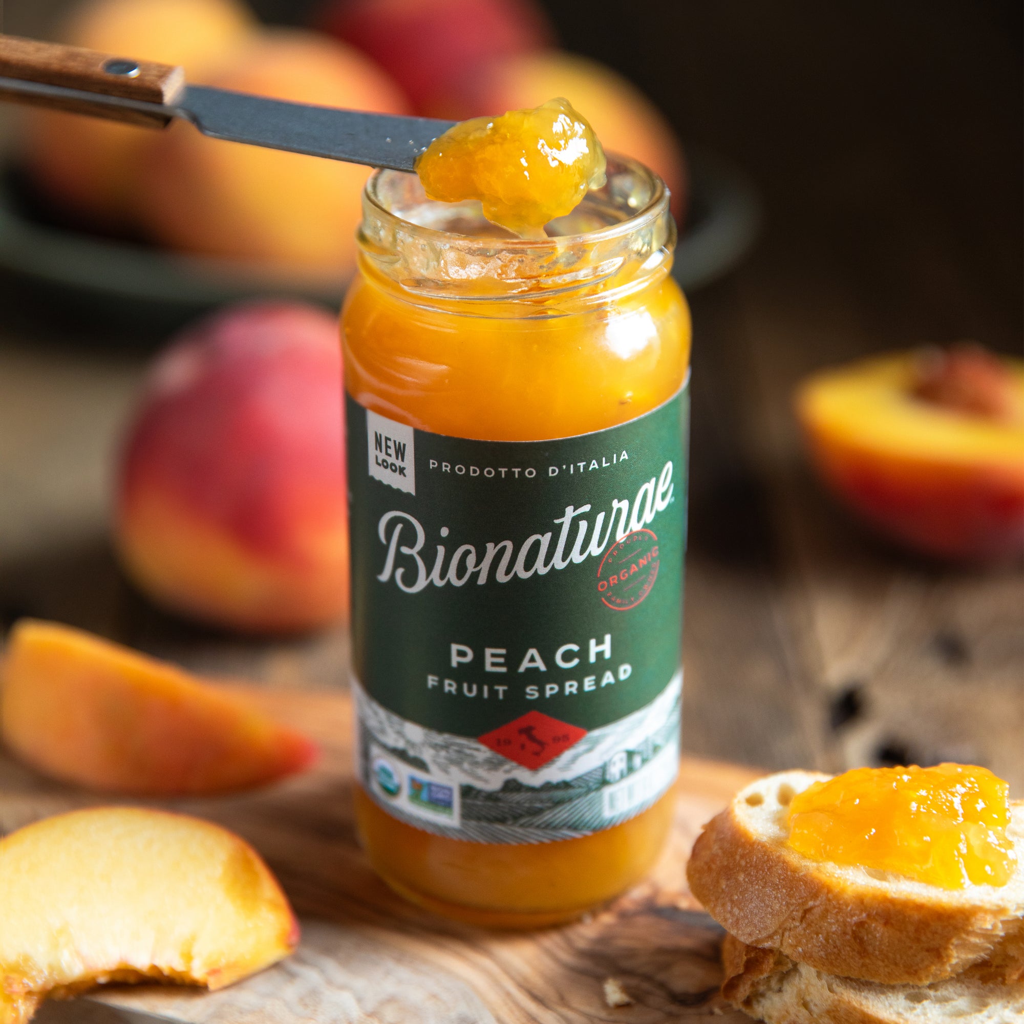 Three-quarter view of 9 oz Bionaturae Organic Peach Fruit Spread jar showing bright spread and sliced peaches on wood