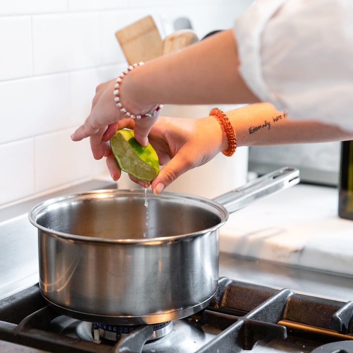 Person squeezing a lime over a saucepan on a gas stove in a home kitchen