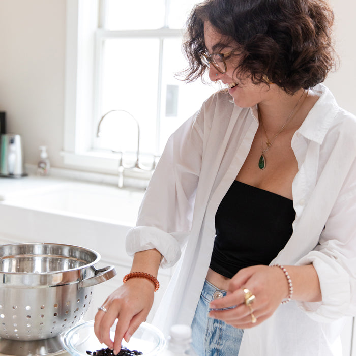 Woman mixing black beans in a glass bowl in a bright home kitchen with a stainless-steel colander on the counter