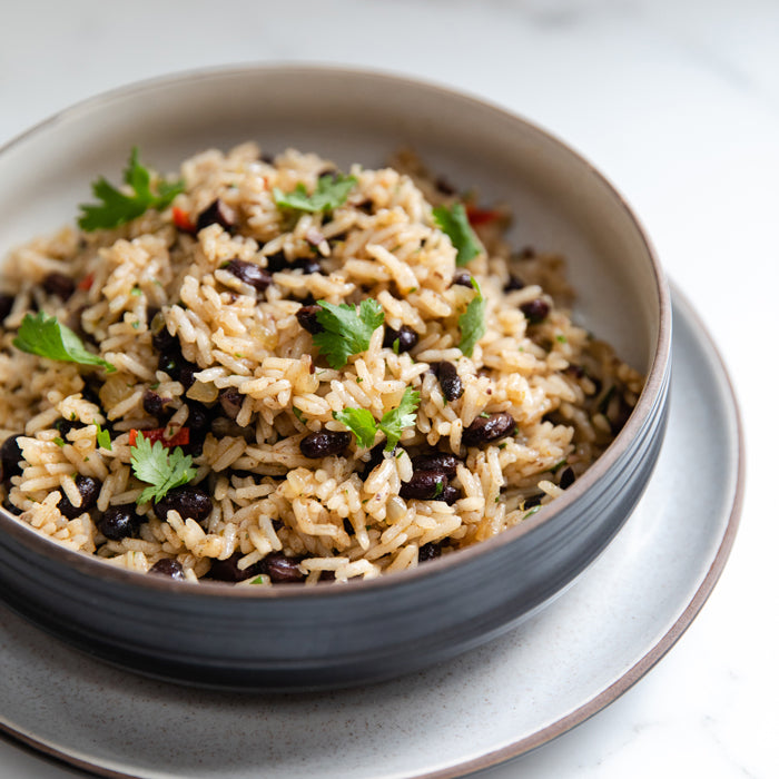 Close-up angled view of a bowl of rice with organic black beans, cilantro, and warm spices on a white marble surface