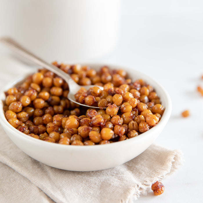 Close-up of cinnamon-sugar roasted chickpeas in a white bowl with a golden, crunchy cinnamon-sugar coating on a linen napkin