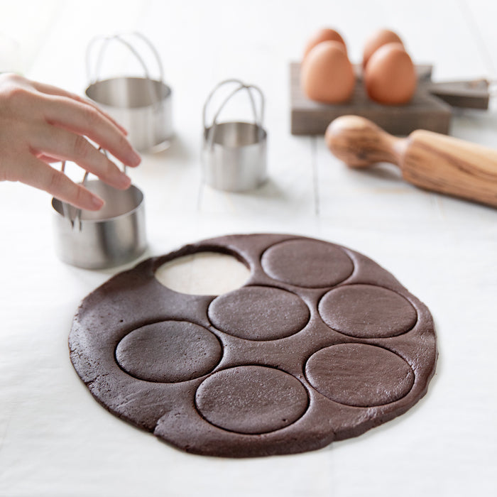 Einkorn chocolate cookie dough being cut into round cookies on parchment paper with metal cutters and eggs