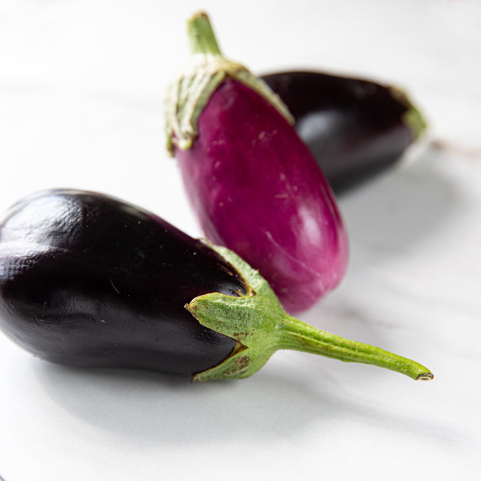 Close-up of three eggplants, one cut lengthwise to show glossy purple flesh on a white marble surface