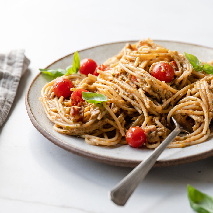 Plate of spaghetti tossed in roasted eggplant and basil sauce with cherry tomatoes, basil leaves, and a fork