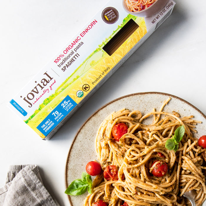 Plate of spaghetti with eggplant sauce and cherry tomatoes beside a Jovial organic einkorn spaghetti box on white background