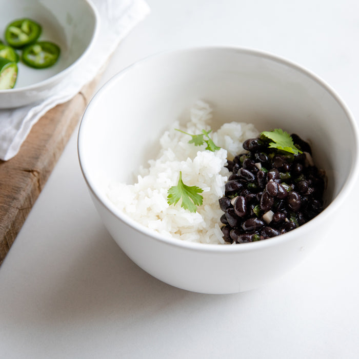 Bowl of white rice with seasoned black beans and cilantro, sliced jalapeño on a small dish at left