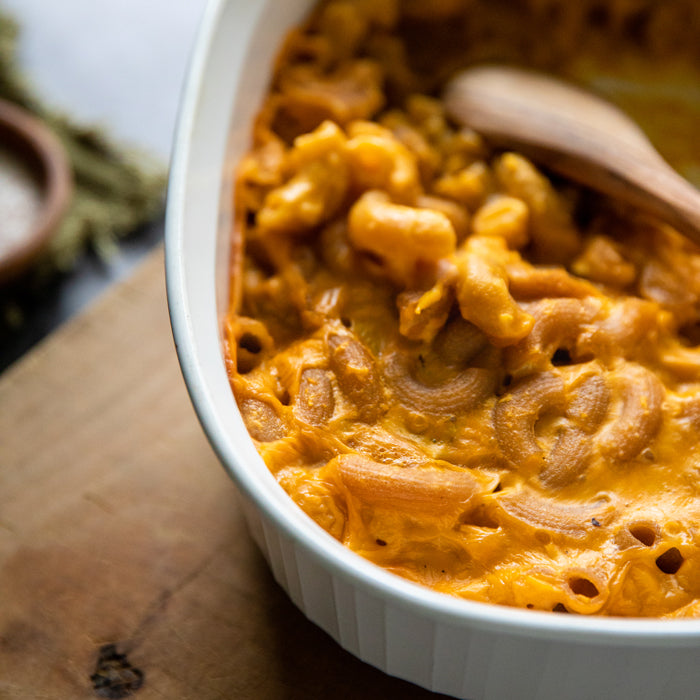 Cauliflower mac and cheese made with Organic cassava elbow pasta in a white baking dish with a wooden spoon