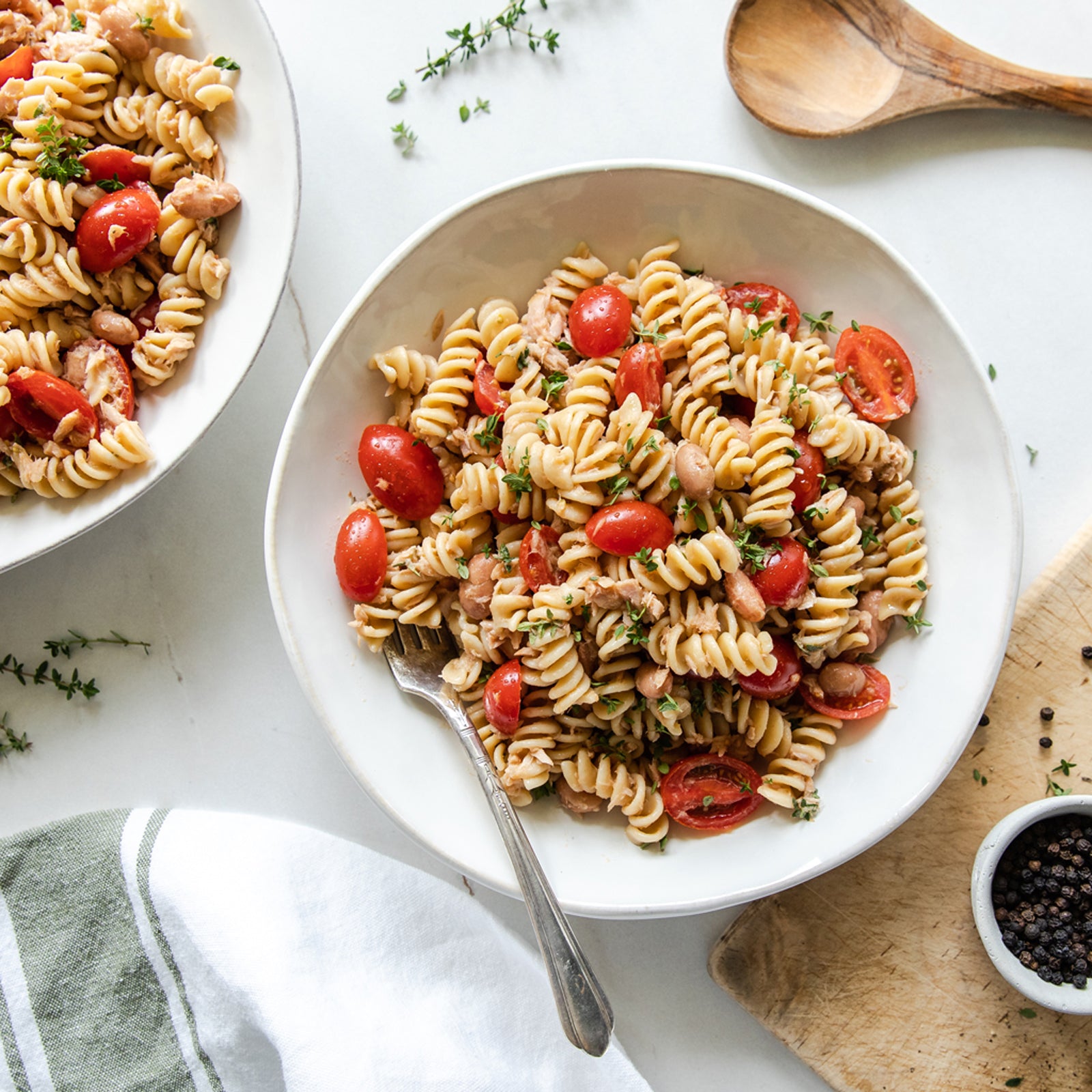 Top-down view of tuna and borlotti bean Einkorn fusilli pasta salad with cherry tomatoes and fresh thyme in a white bowl