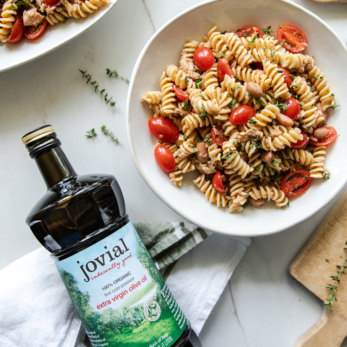 Fusilli pasta salad with cherry tomatoes, borlotti beans and tuna next to a bottle of Jovial extra virgin olive oil