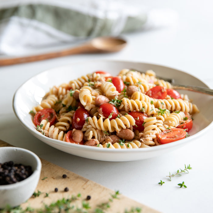 Bowl of Einkorn fusilli pasta salad with tuna, borlotti beans, halved cherry tomatoes and fresh thyme on a light tabletop