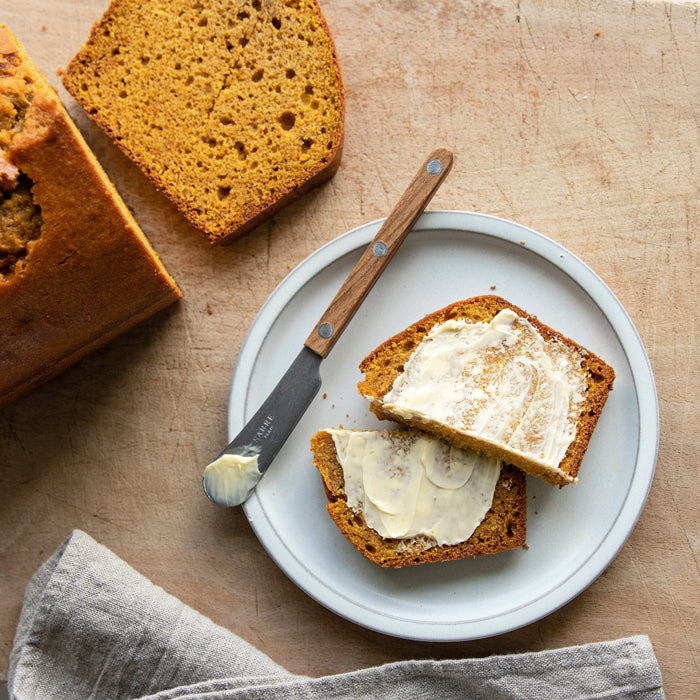Einkorn pumpkin bread slices spread with butter on a plate beside a sliced loaf on a wooden board