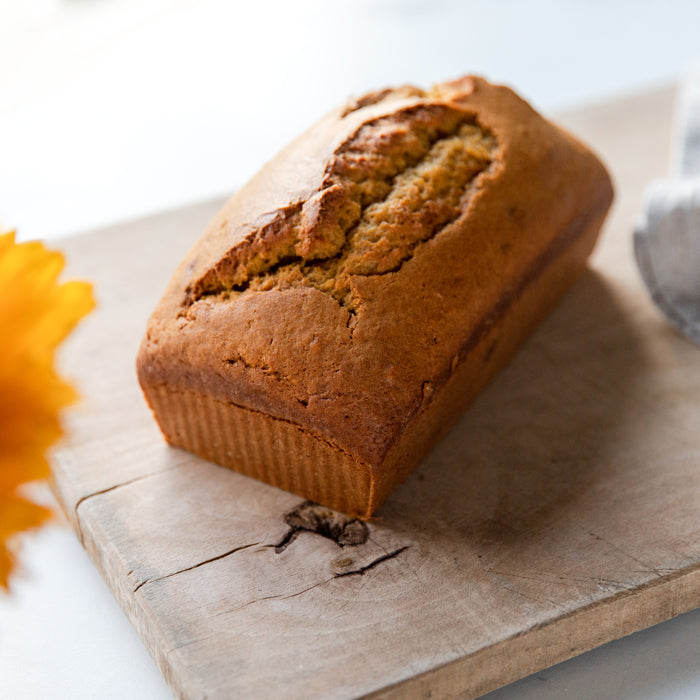 Three-quarter view of an Einkorn pumpkin bread loaf showcasing a cracked golden brown top and ridged sides on a wooden cutting board with soft natural light