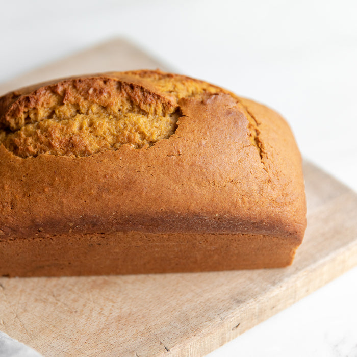 Front-right view of Einkorn pumpkin bread loaf showcasing golden cracked top crust and dense crumb on a wooden cutting board