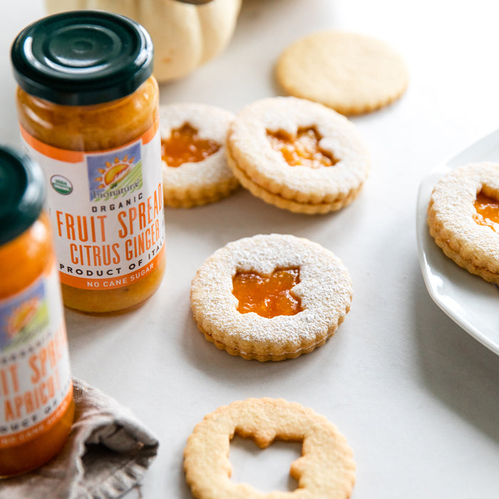 Einkorn Linzer cookies arranged beside jars of organic citrus ginger fruit spread on a light tabletop