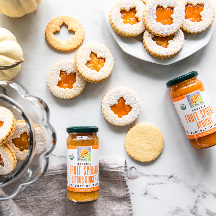 Einkorn Linzer cookies dusted with powdered sugar alongside jars of organic apricot and citrus ginger fruit spread on marble