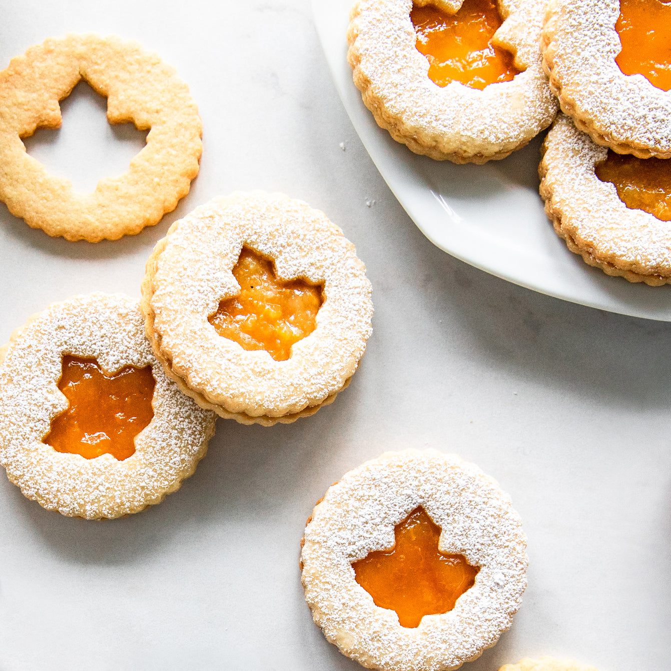 Linzer cookies filled with apricot fruit spread arranged on a white plate