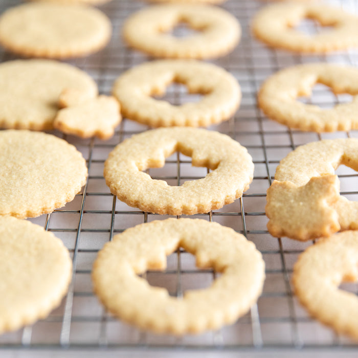 Close-up of round Einkorn Linzer cookies with scalloped edges and cut-out centers cooling on a wire rack