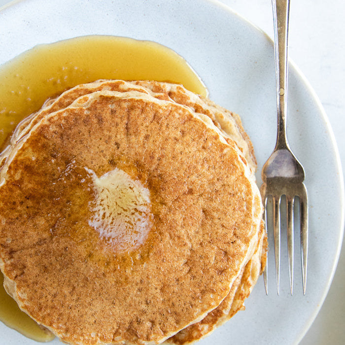 Overhead view of Einkorn sourdough pancakes topped with melting butter and maple syrup on a white plate with a fork