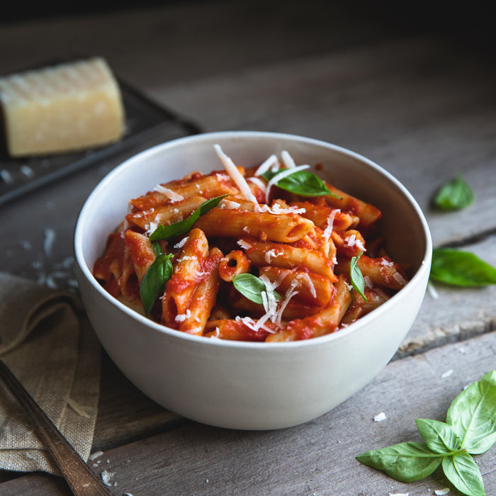 Bowl of organic gluten-free rice and lentil penne tossed in tomato sauce with basil, on a dark wooden table