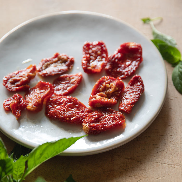 Overhead view of organic sundried tomato pieces showcasing glossy, oil-coated texture on a white plate with basil leaves