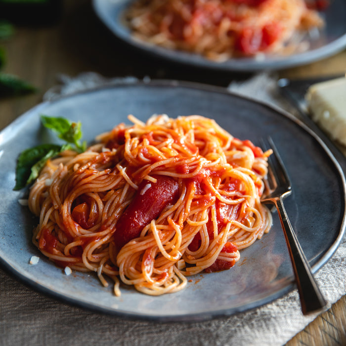 Capellini tossed with tomato fillets and basil on a gray plate with a fork and a wedge of cheese in the background