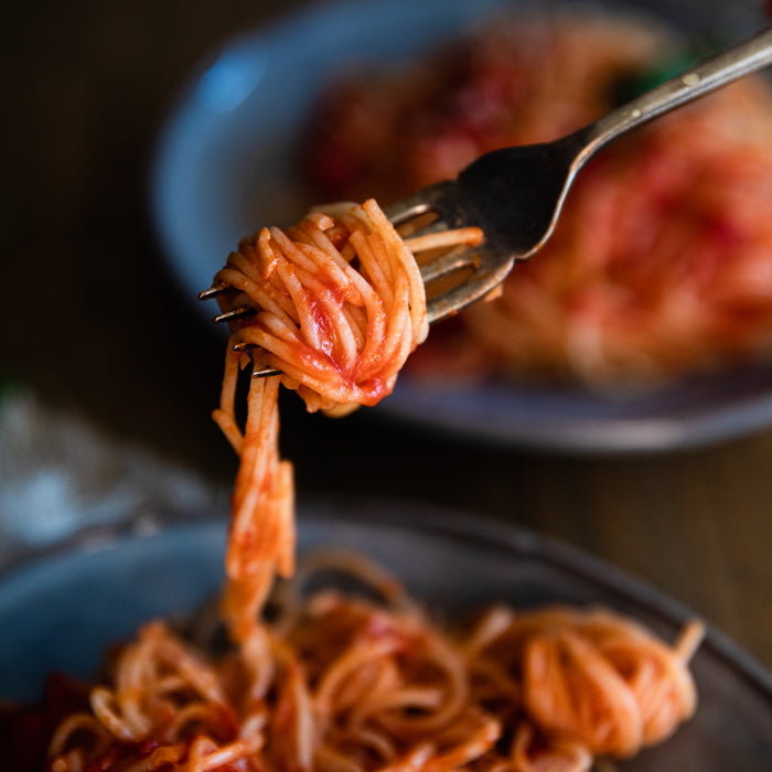 Fork twirling capellini tossed with tomato fillets over a shallow bowl