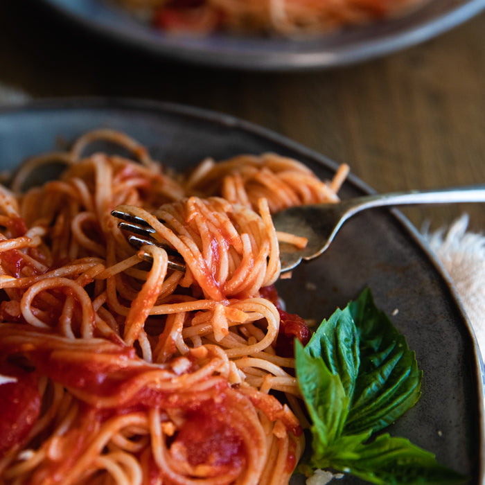 Fork twirling capellini tossed with tomato fillets on a dark plate garnished with fresh basil