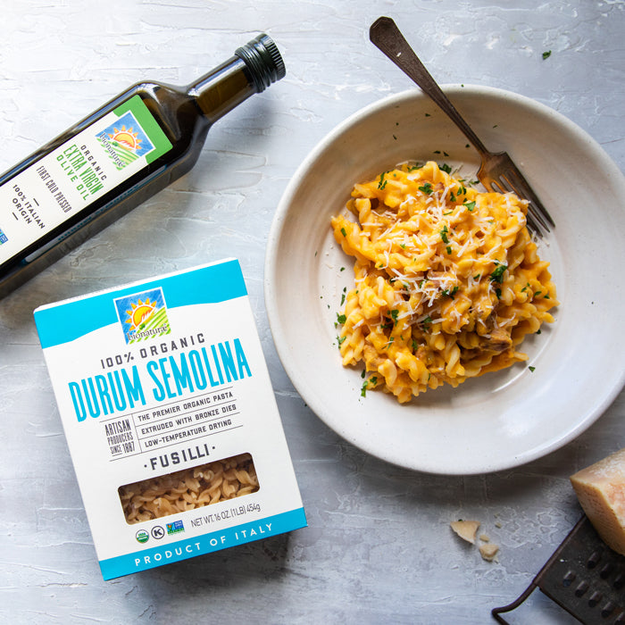 Bowl of pumpkin and sausage fusilli pasta with grated cheese and fork, beside a box of 100% organic durum semolina fusilli and a bottle of olive oil