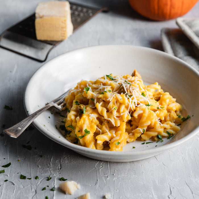 Bowl of organic fusilli in creamy pumpkin and sausage sauce topped with grated cheese and parsley, fork in bowl