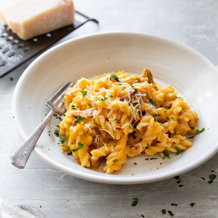 Pumpkin and Italian sausage pasta in a white bowl with creamy sauce, grated Parmesan, chopped parsley, and a fork