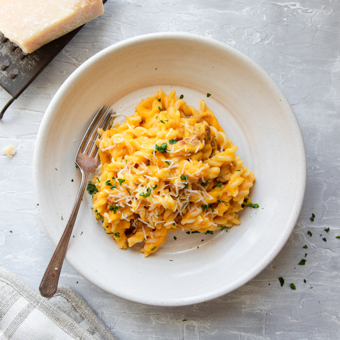 Plate of organic fusilli tossed with pumpkin and sausage, topped with parsley on a light gray surface