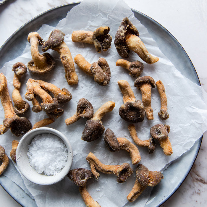 Top-down view of einkorn-fried mushrooms with flaky sea salt on a parchment-lined gray plate