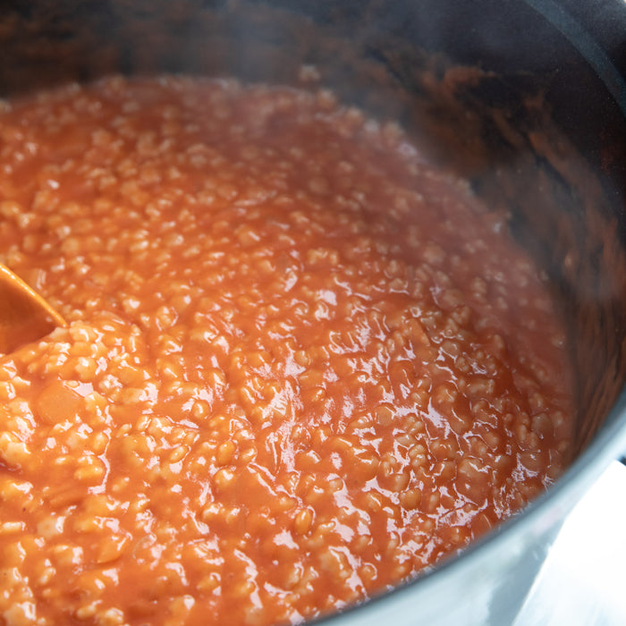 Pot of Brown Rice Stelline pasta simmering in creamy tomato sauce with a wooden spoon