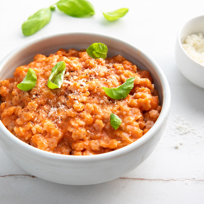 Cooked organic gluten-free brown rice stelline in tomato sauce, served in a white bowl and garnished with basil