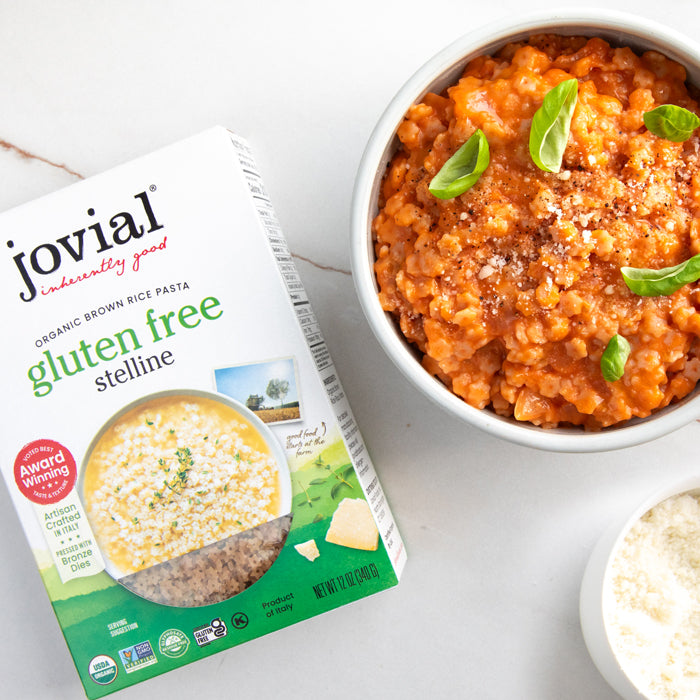 Jovial Organic Gluten Free Brown Rice Stelline box beside a bowl of stelline pasta in tomato sauce on a light countertop