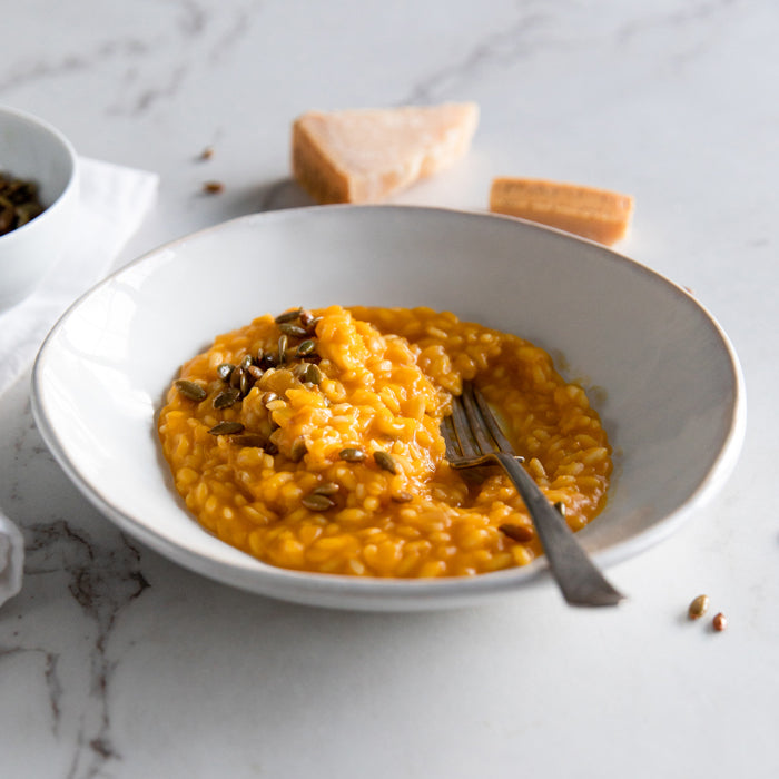 Top-front view of butternut squash risotto showing creamy saffron-orange rice garnished with toasted pepitas in a white bowl on a marble countertop